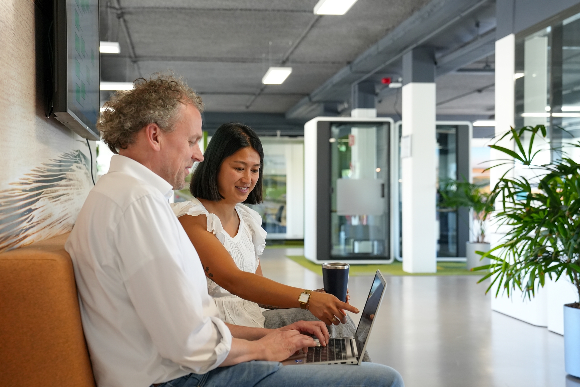 Twee collega's op een bank die samen naar een laptopscherm kijken tijdens een informeel overleg.