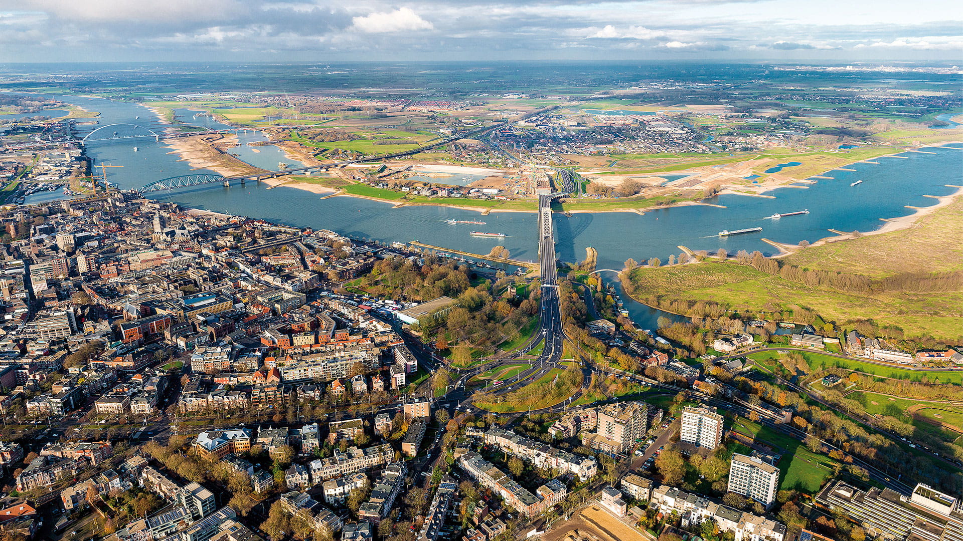 Aeriale foto van een stad met een brede rivier en een lange brug die stedelijk gebied verbindt met groen landschap.