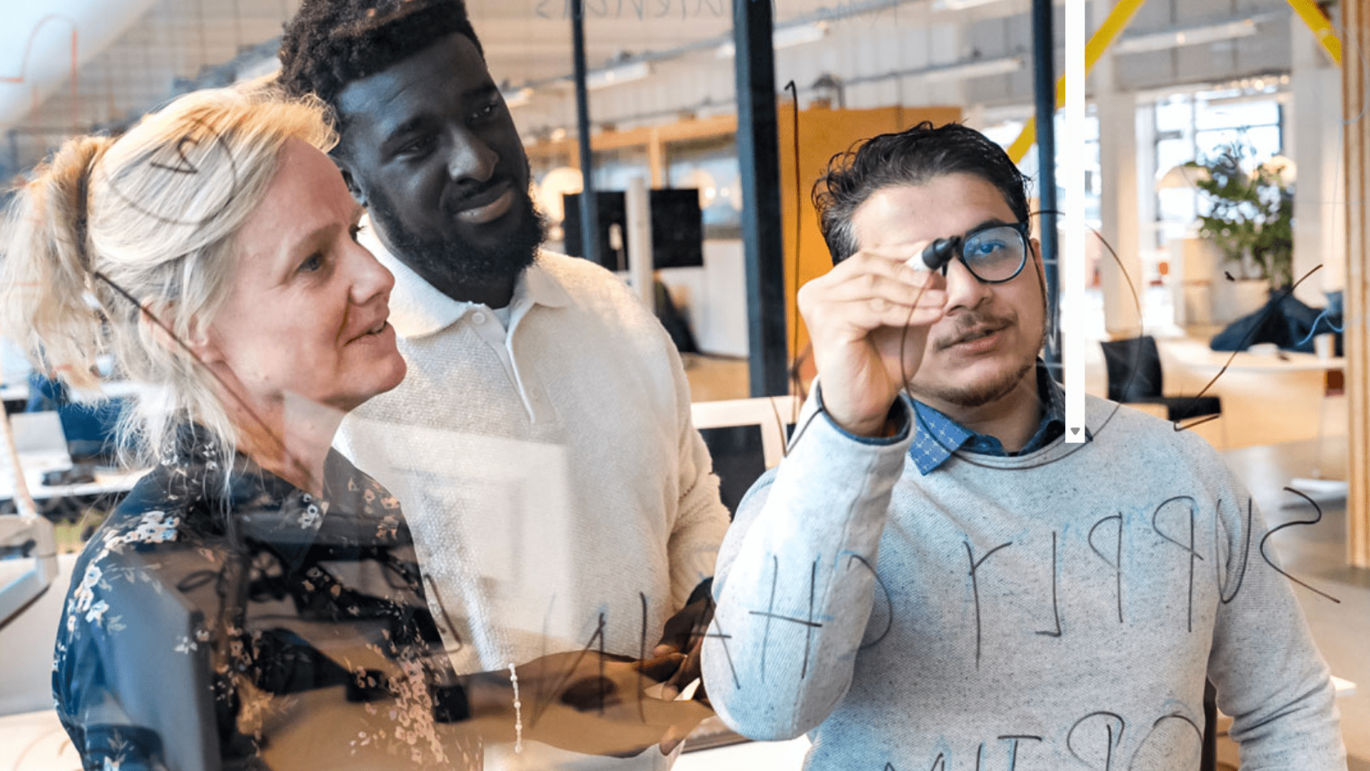 Drie collega's zijn samen aan het brainstormen op een glazen wand
