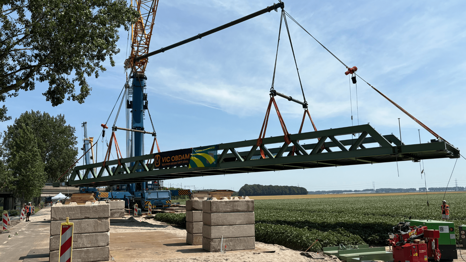 Foto van een kraan waaraan een fietsbrug hangt zodat deze kan worden geplaatst