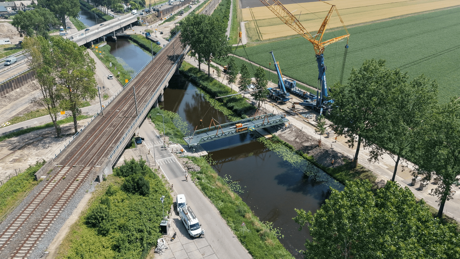 Luchtafbeelding waarbij een fietsbrug door een kraan op zijn plek wordt gelegd