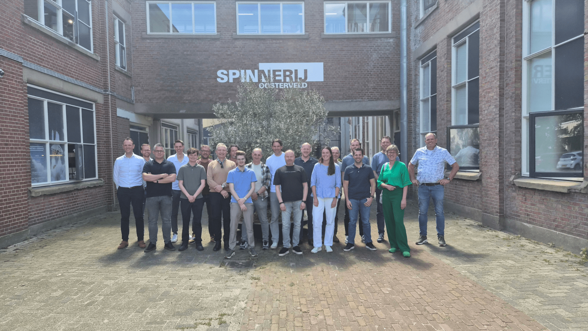Groep van ongeveer twintig professionals staat in een binnenplaats voor het gebouw “Spinnerij Oosterveld” in Enschede