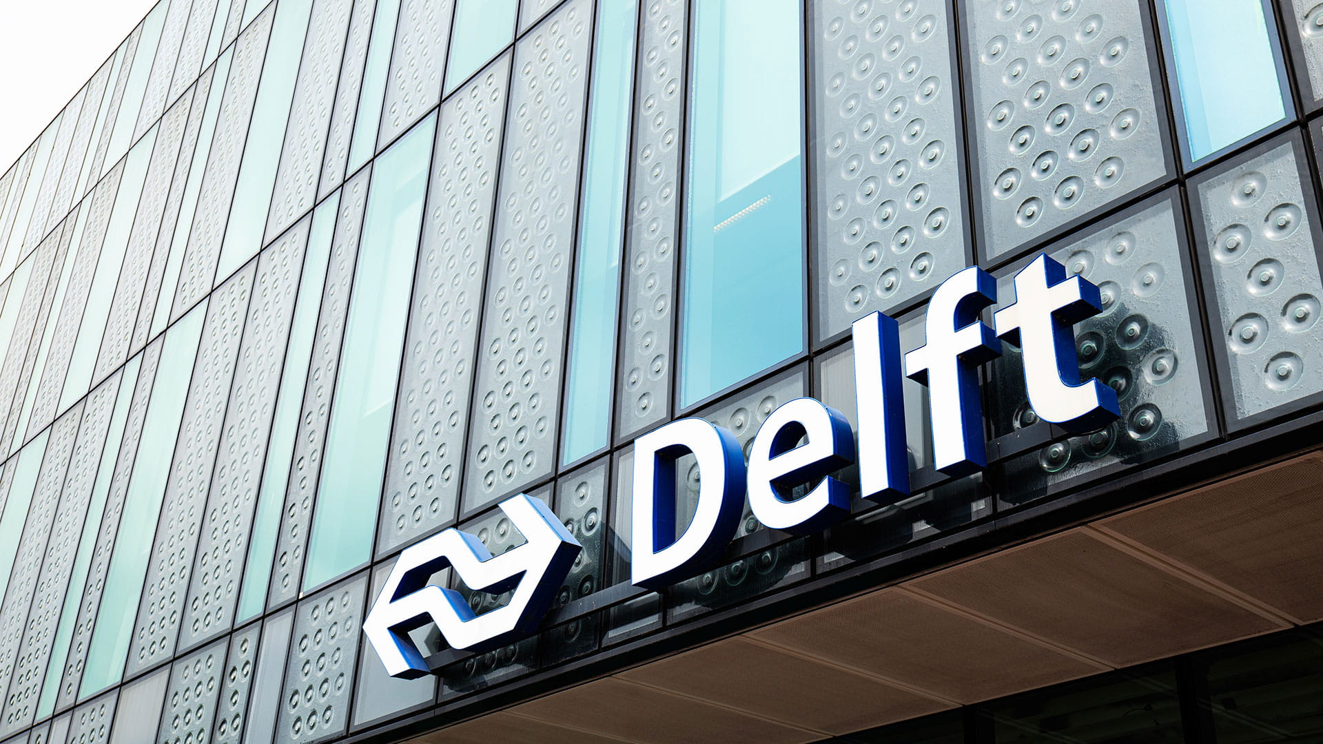 Delft and NS logotype writing on the glass facade of the main building entrance.