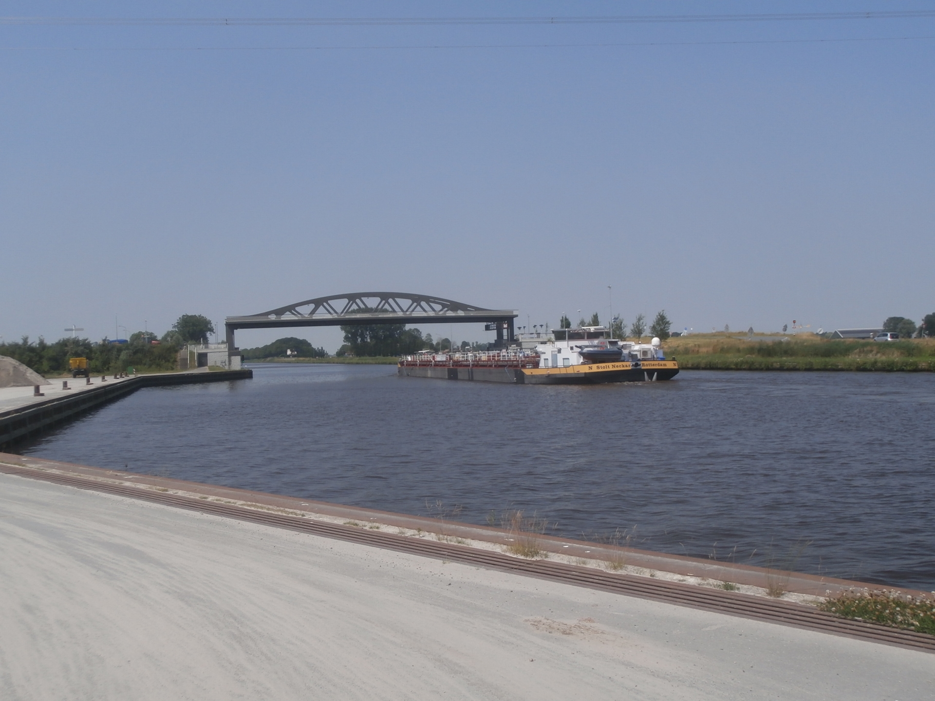 Een groot binnenvaartschip passeert een markante boogbrug op de Hoofdvaarweg Lemmer-Delfzijl, een vitale logistieke schakel voor internationaal transport naar Duitsland.