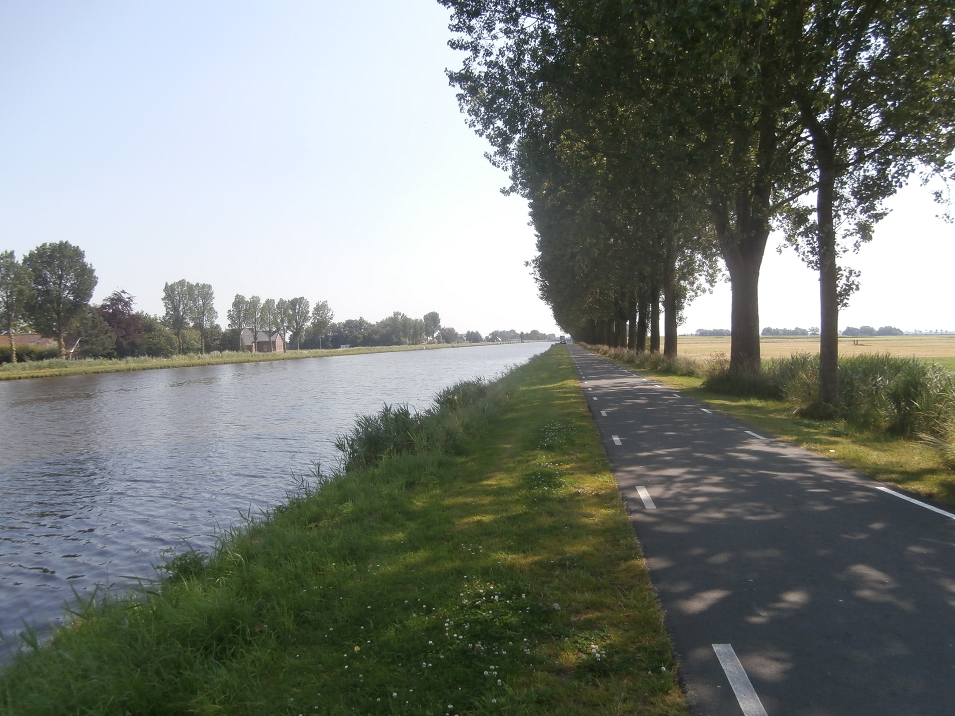 Een strak fietspad onder een schaduwrijke bomenrij flankeert het kabbelende water van deze 118 kilometer lange vaarroute door het Noord-Nederlandse landschap.