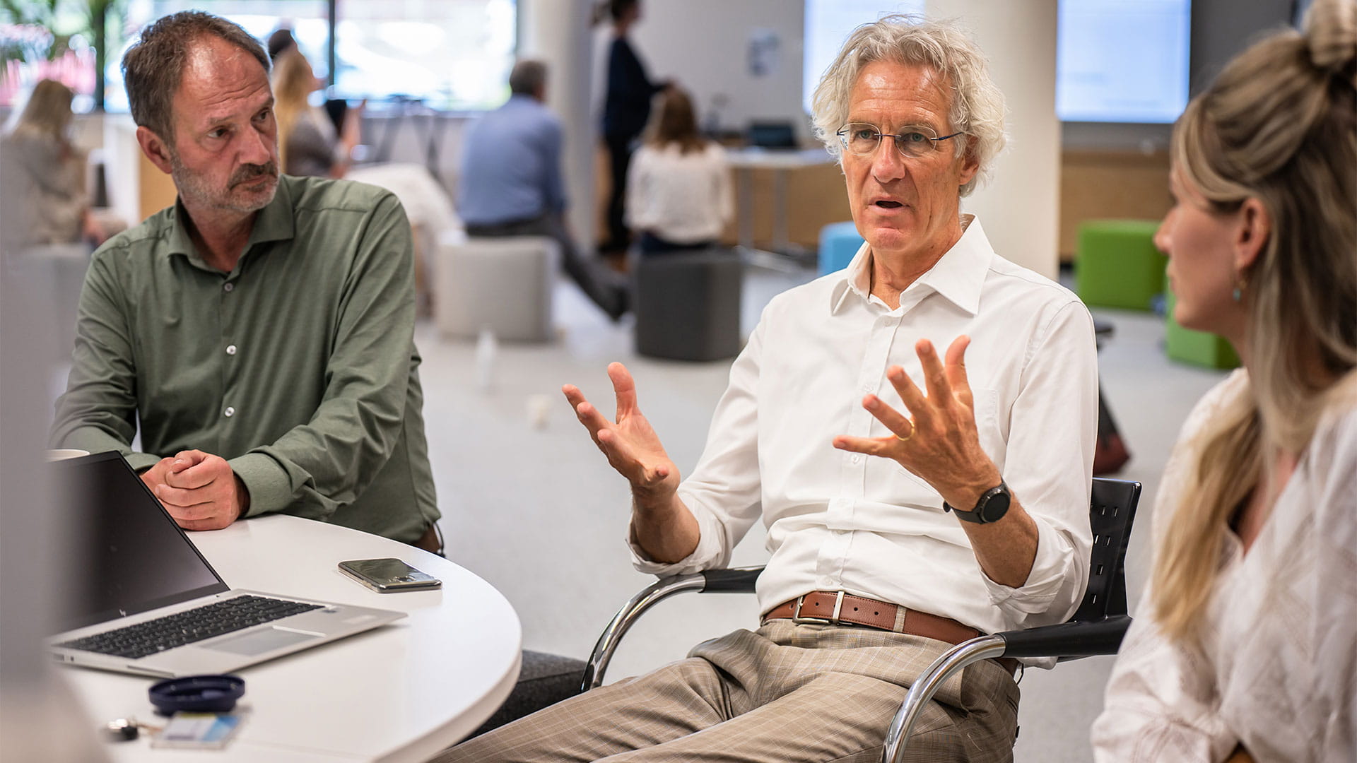 Drie mensen aan het praten aan een tafel met laptop